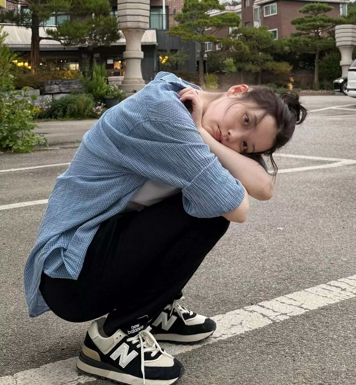 IU這套私著把最基本的單品,穿出了記憶點。她以淺藍色條紋襯衫內搭白T,下身選擇黑色長褲,整體配色乾淨俐落,又因為藍、白、黑三色的堆疊,讓簡單穿搭多了幾分層次。腳上搭配黑白配色的New Balance574,剛好呼應整體中性又帶點復古感的基調,也讓造型看起來更有份量。這種穿法厲害的地方就在於,不靠複雜單品也能很有氛圍,特別是IU蹲坐的姿態、微亂髮絲與近乎素顏的狀態,是一套愈看愈耐看的日常範本。