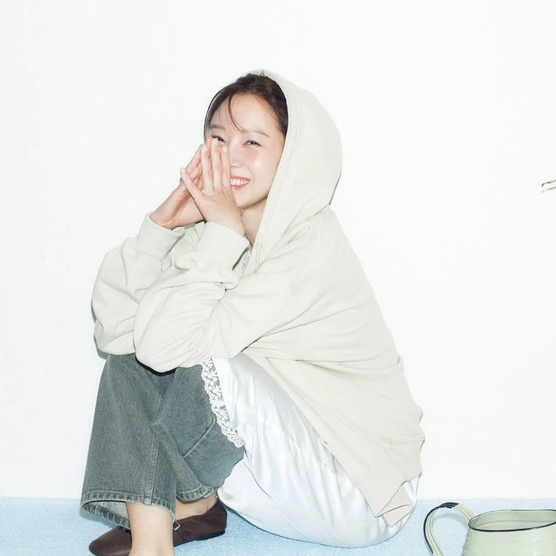 選擇米色帽T搭配淺色牛仔寬褲，整體配色維持在柔和的大地色調，看起來自然又不會過於休閒。內搭白色長版上衣，側邊微微露出蕾絲下擺，替簡單造型多了一點細節層次。寬鬆帽T搭配直筒牛仔褲的輪廓，讓整體比例依然俐落，不會被寬鬆感吞沒。