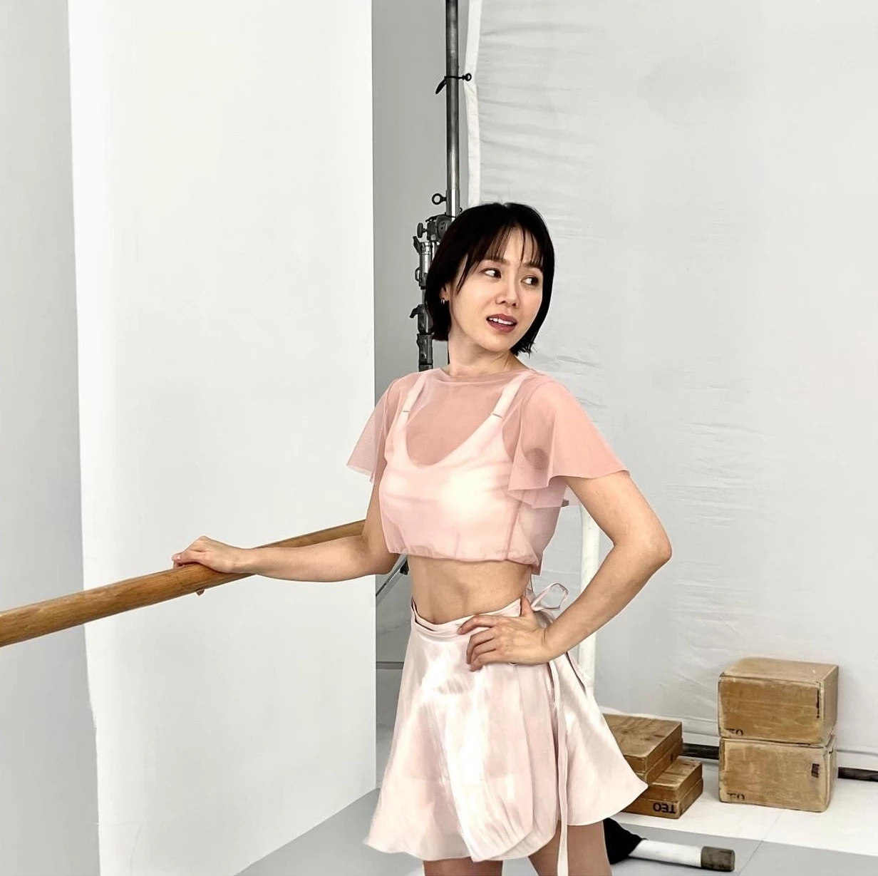 第三招就是要跟「蝴蝶袖」說再見!孫藝珍這套以一件粉色紗質短袖上衣,罩在內層的背心之外,下身搭配粉色緞面短裙,甜美又有層次。這套最聰明的地方,就是那對飄逸的短袖——它剛好蓋住最容易顯胖的上臂外側,紗質的透膚感又不會顯得厚重悶熱,比無袖背心更能修飾手臂線條,是怕露蝴蝶袖、又想穿得清涼的人最值得學的一招。想露膚又想遮手臂,用「背心+紗質短袖罩衫」的疊穿法就對了
