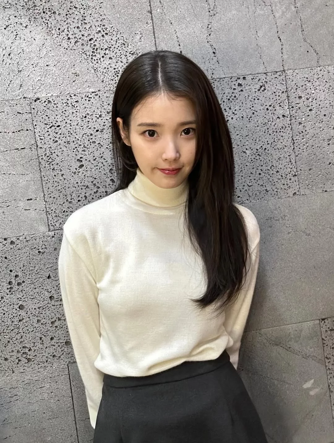 這一套可以說是最精準的「顯白範本」針織穿搭。IU選擇的是偏奶油調的象牙白高領針織,不是冷白、也不是米黃,而是一種在室內光線與自然光下都很穩定的柔白色。