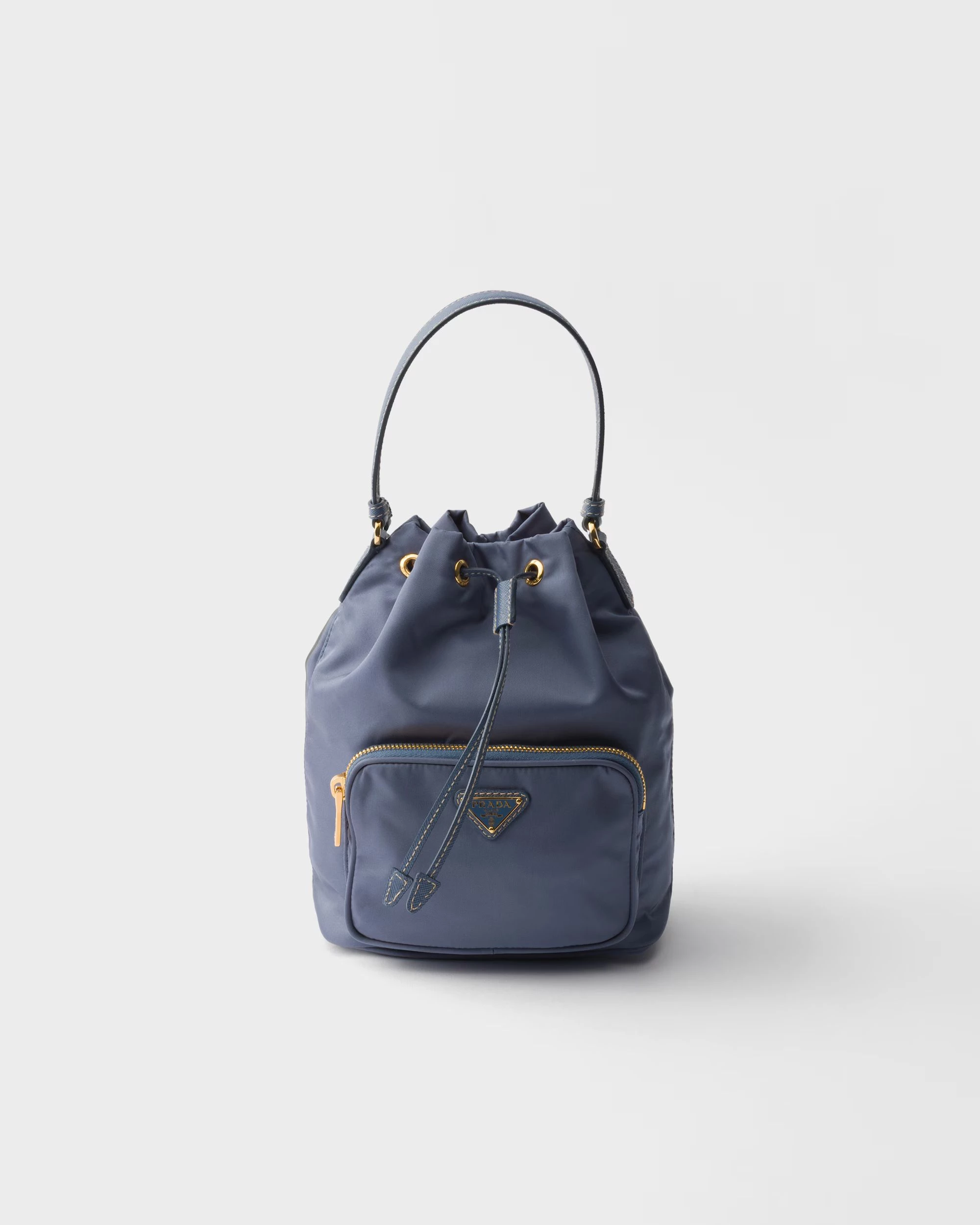 Prada Duet水桶袋第一眼會被它的「輕」吸引。Re-Nylon 的材質帶一點自然垂墜，背在身上不會撐出厚重感，反而有種貼著身體走的流動線條。包身偏柔軟，但不至於失去形狀，抽繩收口後會形成一個很順的弧度。外側拉鏈口袋也很實用，卡片或鑰匙可以直接拿取，手提時俐落，換成斜背又多一點日常感。這顆的重點在於，它很輕鬆，但依然優雅。