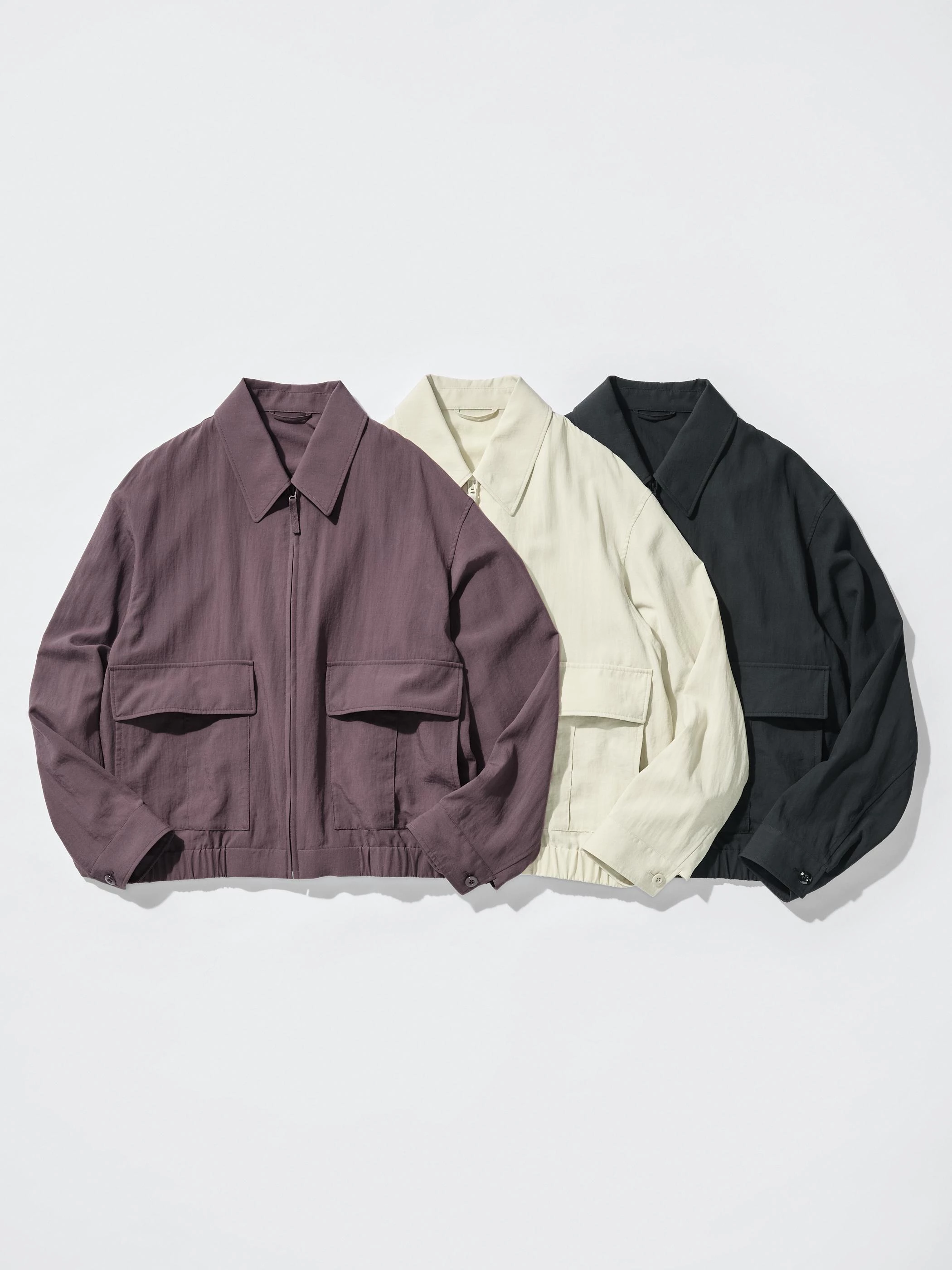 另一款短版布勞森外套則更強調中性輪廓。設計延續 Uniqlo U 標誌性的寬版領片，領型略帶工裝感，但線條乾淨俐落，使整體風格介於休閒與都市之間。外套採用隱藏式拉鍊設計，外觀更加簡潔，同時搭配織帶拉鍊頭增加操作便利性。腰部雙層翻蓋口袋是這件單品的亮點之一，從上方或側邊都能放置物品，兼具實用與造型。袖口以釦式收束，讓袖型更有結構感。藕紫、象牙白與黑色三種配色都偏向低調耐看的色系，適合男女共穿。若想營造較為現代的輪廓，可搭配寬版長褲或短褲，讓整體比例更俐落。