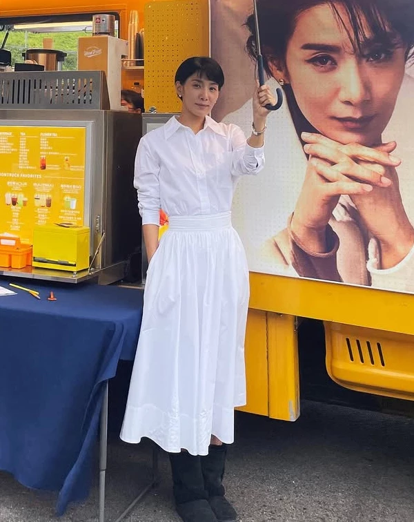 同樣是在應援餐車前,金瑞亨卻展現了少見的全白知性造型。上身是乾淨的立領白襯衫,下身搭配一條帶有細緻抓褶設計的高腰白色A字長裙,腳下則踩著一雙黑色休閒短靴。全白色調,不僅在視覺上極具延伸感,更在隨性中注入了一抹優雅的文藝氛圍。