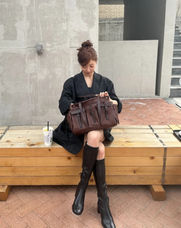 李世榮完全就是把「甜酷風」玩到極致的範本。上半身是一件設計感十足的蓬鬆黑色西裝外套，大大的領口露出鎖骨，看起來有點小女人的優柔，頭髮還綁了個超可愛的丸子頭，單看上半身，這絕對是走甜美路線的。但下半身，她反而大膽地配上了一雙過膝的黑色皮筒靴，露出那一段恰到好處的膝上處。這雙靴子的挺闊感跟上半身的蓬鬆感形成強烈對比，瞬間把甜美度轉化成一種甜美的的率性。