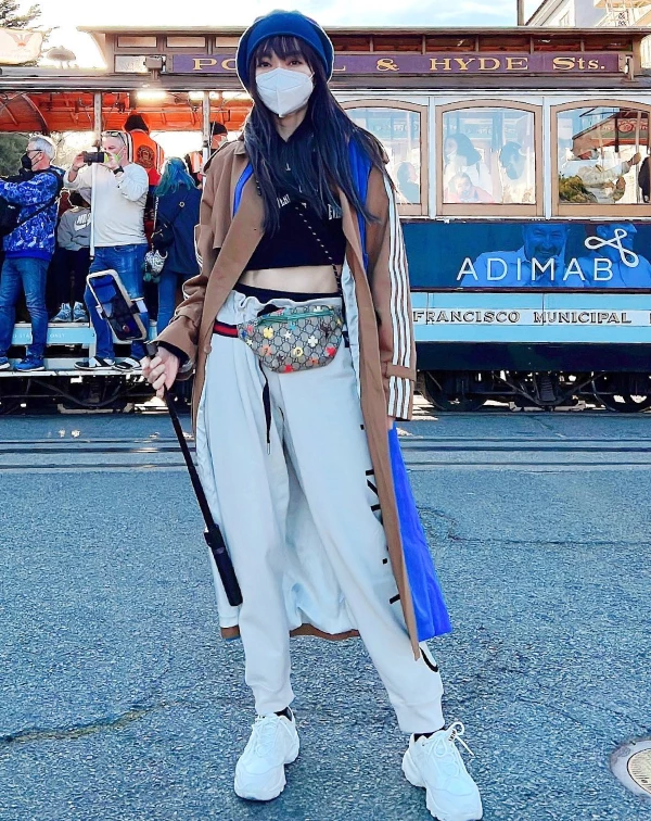 謝金燕在舊金山叮叮車前的街拍，簡直是高階減齡的教科書！要穿出這種少女感與氣場並存的風格，核心就在於「單品之間的混搭」，外套選用略帶挺廓的焦糖色經典風衣撐出氣場（三條線的設計，估計是Gucci與Adidas之前聯名）；內搭，卻大膽疊穿Crop Top 短版內搭，這種衝突感直接打破長版大衣的成熟魔咒。再配上高腰縮口運動褲，不只能拉長腿部線條，更散發一種健康活力；最後再用亮藍色毛帽與繽紛印花腰包點綴，讓視覺重心上移並增添街頭潮感，完全展現出「逆生長」的生活態度！