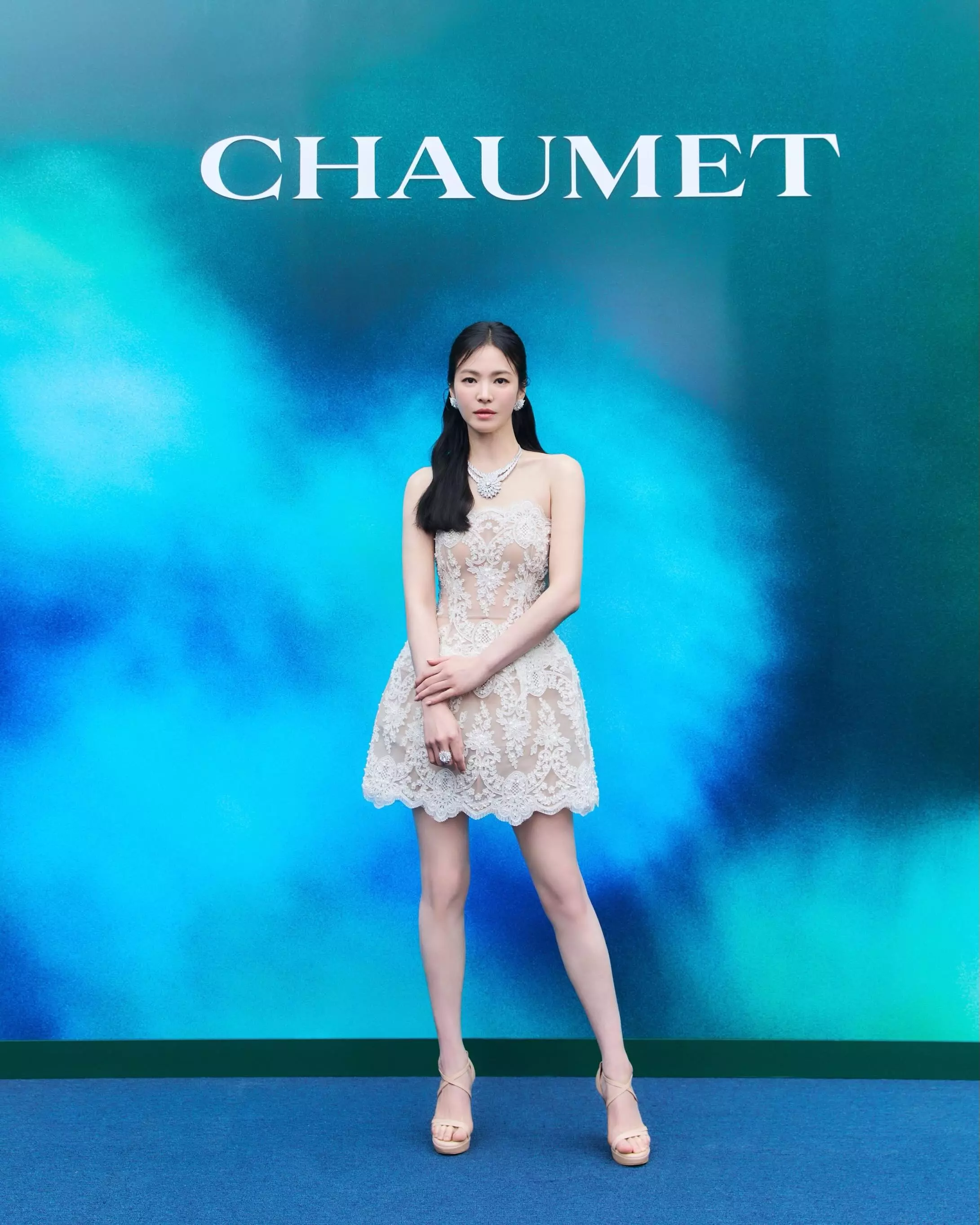 出席Chaumet珠寶活動，宋慧喬以一件米白色蕾絲抹胸迷你洋裝搭配同色系米膚色踝帶高跟涼鞋，全身從頸間鑽石頸鍊到腳尖的色調高度統一，創造出最強的視覺腿長效果。踝帶涼鞋選擇「裸膚色系」是這套的勝負手：鞋面與肌膚融為一體，雙腿的延伸感毫無中斷，視覺腿長比黑色同款至少多出10公分。配上迷你裙大量露腿，被Chaumet珠寶點綴的鎖骨與頸線更顯優雅成熟，是同時達到「性感」與「減齡」的高難度示範。