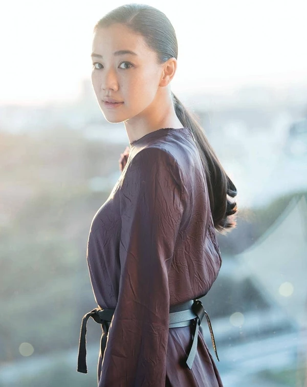 蒼井優穿著一襲深紫褐色的長袖洋裝，面料帶著細緻的自然壓褶與微光感，腰間隨性繫上一條黑色皮革寬腰帶。整體造型沒有一絲贅飾，透過微光面料與收腰剪裁，在成熟、沉穩的色調中，展現出俐落又神清氣爽的年輕體態。