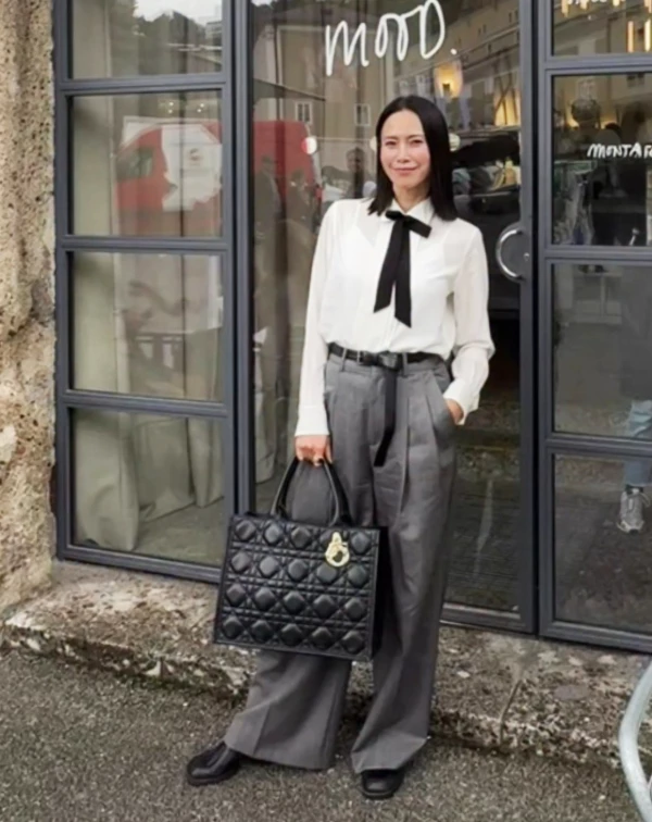 想穿出「知識份子」的高級感，搭法就在細節中。略帶透膚感的絲質襯衫，本身就很溫柔，但加上一條繫上的黑色緞帶領結，立刻多了點中性的帥氣。下半身，則是搭配高腰灰色打摺褲與皮帶，將腰線拉高、營造乾淨俐落的優雅氣質。一般人若想要把這條褲子穿好。如果身材不是那麼瘦，皮帶可以選細一點的，且褲管記得捲起來露出一點腳踝。就能「無痛拷貝」到日常辦公室。