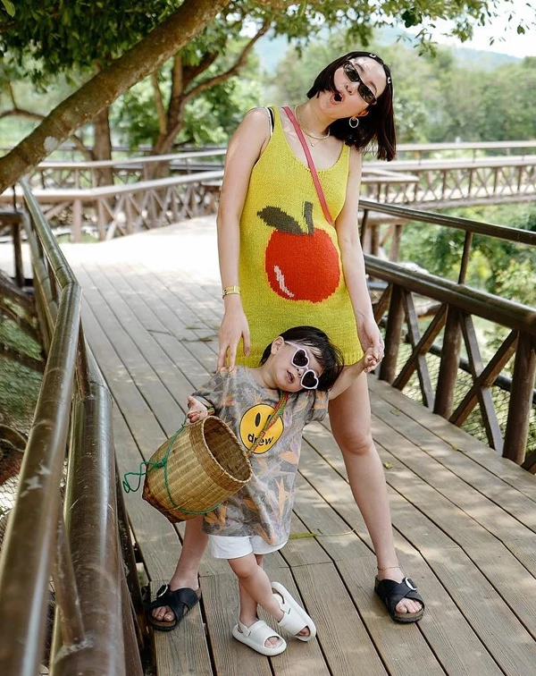 這套親子裝真的是可愛到讓人融化！Melinda再次證明了她「玩色達人」的稱號絕非浪得虛名。高明地將原本容易顯得童稚的可愛元素，轉化為大膽且充滿玩心的時尚宣言！最吸睛的，絕對是亮黃色的針織背心裙中央那個巨大的紅色蘋果圖案，這不僅是一個強烈的視覺焦點，更奠定了整體造型俏皮、純真的基調，瞬間讓可愛風多了一份時髦的層次感，完全打破了傳統配色框架。