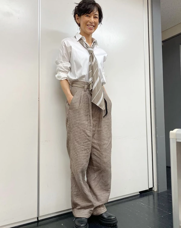 鈴木保奈美將看似乖巧的白襯衫與高腰千鳥格紋寬褲組合,卻高明地解開領口、將袖子隨意捲起,並配上一條大地色系的寬領帶。一般人穿白襯衫與格紋褲最怕像制服或顯老,我們可以學她故意不把領帶打得太嚴謹,讓它像圍巾般鬆散地掛在頸間,再踩上一雙硬挺的黑色厚底樂福鞋或短靴,就能瞬間拉滿英倫學院風的帥氣,巧妙達到減齡效果。