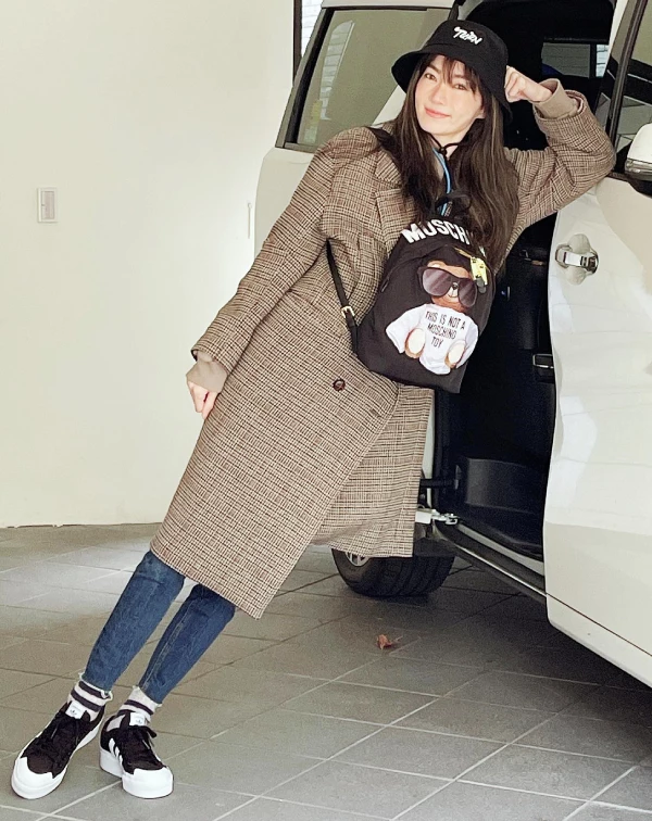 這張穿搭照，則完美示範了謝金燕是如何透過「反差萌」來達成減齡效果的！她將知性成熟的長版格呢大衣，大膽混搭上童趣十足的Moschino小熊背包與黑色漁夫帽，成功將整體氛圍從嚴肅的英倫學院風，轉化為俏皮又充滿活力的街頭少女感。