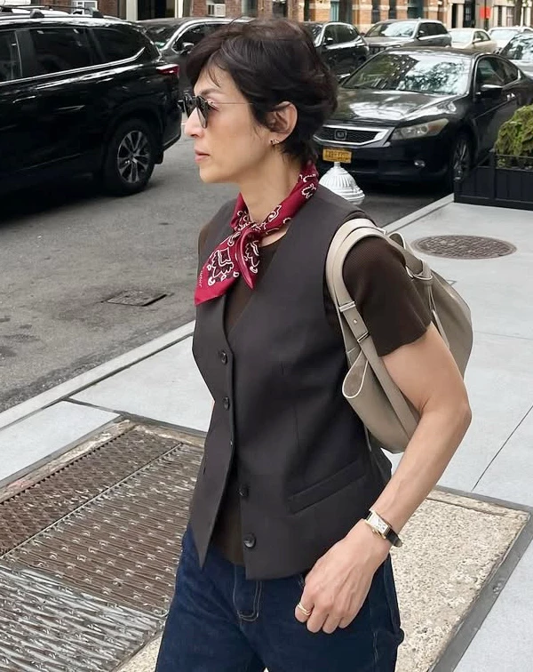 在紐約街頭,鈴木保奈美以深咖啡色西裝背心內搭同色系短袖上衣,下身搭配休閒牛仔褲,最亮眼的,絕對是頸間那條復古絲巾。當我們穿著大範圍的深色、大地色系或基本款正裝時,秘訣就在於加入高對比的配件。學她在領口繫上一條鮮豔的印花小方巾,並配上一副百搭的黑色墨鏡,不僅能一秒聚焦視覺、修飾頸部線條,更能為沉穩的穿搭注入滿滿的美式復古活力。