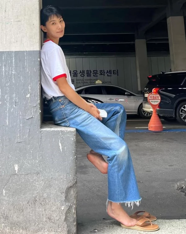 想要呈現鄰家姐姐的無壓迫感,這套請直接拷貝!一件簡單的滾邊白T,搭配一條刷色自然的九分微喇叭牛仔褲,褲腳的抽絲細節多了一絲不羈。她甚至連鞋子都選了最放鬆的皮革夾腳涼鞋。這種極致慵懶的穿搭,反而襯托出她清爽的短髮與乾淨的面容。減齡不需要層層堆疊,有時簡單點搭配,反而能讓人看起來年輕10歲。