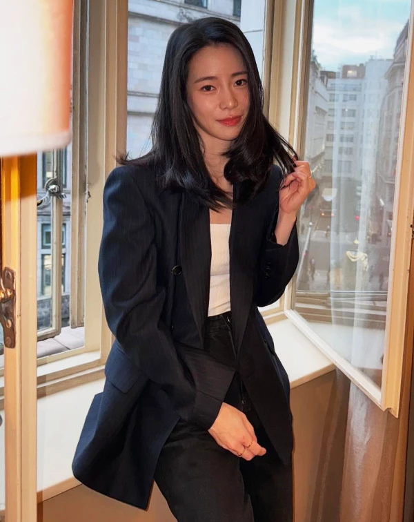 如何將正式的西裝外套穿出「非正式」的高級感?林智妍在這套穿搭中給出了完美答案。她選用了一件深藍近黑的細條紋西裝外套,這種帶有微光澤感的材質,比起純黑色更具深度及質感。內搭則選擇了一件輕鬆的純白平口上衣,透大面積的鎖骨留白中和了西裝的沉重感,不僅展現了微性感的女人味,更體現了時下最流行的「剛、柔並濟」風格。這種「不過度用力」的時髦,正是職場女性們在出席晚宴或重要聚會時,最能展現自信、大氣風範的搭配參考。