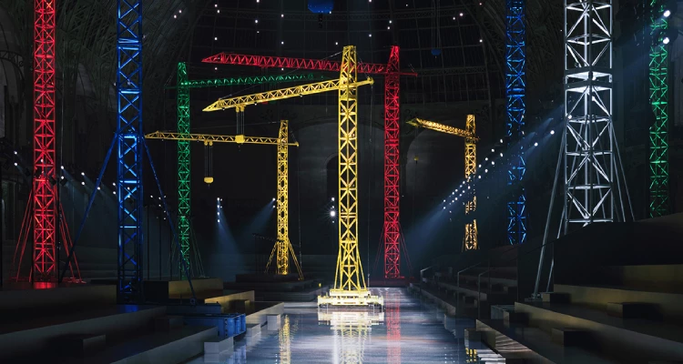 從參與嘉賓收到的2026秋冬大秀邀請函「一把可折疊的量身小尺」，就能感受到2026秋冬秀場的巧思。走進秀場，目光不自覺被散落在四周的大型裝置吸引，那些造型彷彿橋式起重機或港口吊臂的裝置，呼應了秀場佈置的工業氣息。