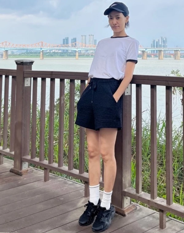 金瑞亨穿著簡單的白T恤,搭配黑色高腰運動短褲,最絕妙的細節在於她腳上的黑色運動鞋與那雙拉得高高的「純白長襪」,長襪的加入立刻注入了美式復古運動員的活力,完全消除了大齡女子穿短褲可能帶來的居家感。想要運動風不顯邋遢,細節配件(帽子與襪子)絕對是關鍵!不僅能修飾腿型,還能增添日、韓流行的街頭少女感。