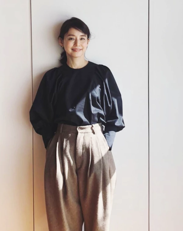 這套造型，真的很有石田百合子予人的那種「優雅又高級」的風格！她用黑色燈籠袖上衣，搭配燕麥色高腰抓褶褲，看起來沉穩卻完全不顯老。尤其她將上衣紮進高腰剪裁的褲子裡，讓整體比例瞬間變超好，也讓人看起來更俐落有精神；微微澎起的袖型，則替黑色增加一點柔和少女感。其實…減齡不一定靠粉嫩色系，像這種大地色＋有線條感的搭配，反而更能穿出成熟又年輕的時髦感。