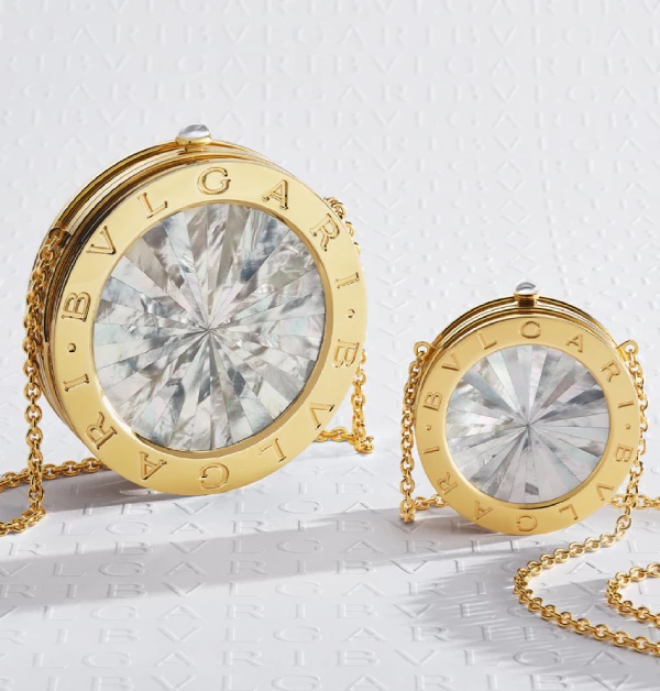 以鍍金鋁和黃銅圓柱形包身勾勒出建築般的雕塑感。正面閃耀著珍珠母貝鑲嵌的放射狀扇形圖案，不僅呼應寶格麗經典的珠寶語彙，搭配可折疊收納的24K鍍金鍊帶，更讓這件作品在手拿與肩背之間，散發出優雅且深具當代感的藝術氣息。（商品價格店洽）