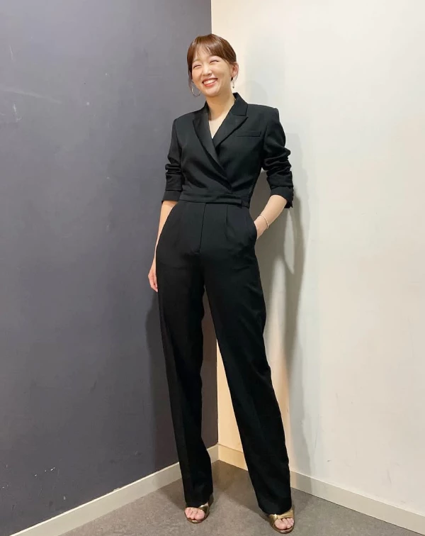 秦基周也能展現出截然不同的減齡風格。她穿著全黑的西裝套裝，但褲子是寬鬆的寬褲版型，打破了傳統西裝的沉悶感。想要將西裝穿出年輕感，重點在於「放鬆」。選擇版型偏大或寬褲造型的西裝，並搭配休閒的鞋款（如涼鞋、運動鞋），就能平衡西裝的正式感，展現出自信大氣的都會女性魅力。