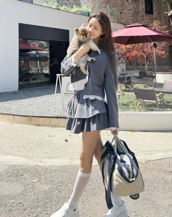 帶愛犬出門散步的李多海,選擇了一套帶有法式浪漫細節的灰色套裝。短版外套的邊緣,巧妙拼接了白色蕾絲,平衡了西裝面料的硬挺感,為臉部周圍增添一抹溫柔光暈。下半身搭配高腰的百褶傘狀短裙,蓬鬆的裙擺,正是極佳的藏肚利器,搭配白色中筒襪與厚底休閒鞋,既能減輕孕期雙腿的負擔,又能延伸腿部線調。整體色調清爽,完美示範了如何將「孕婦裝」穿出甜而不膩的高級少女感。