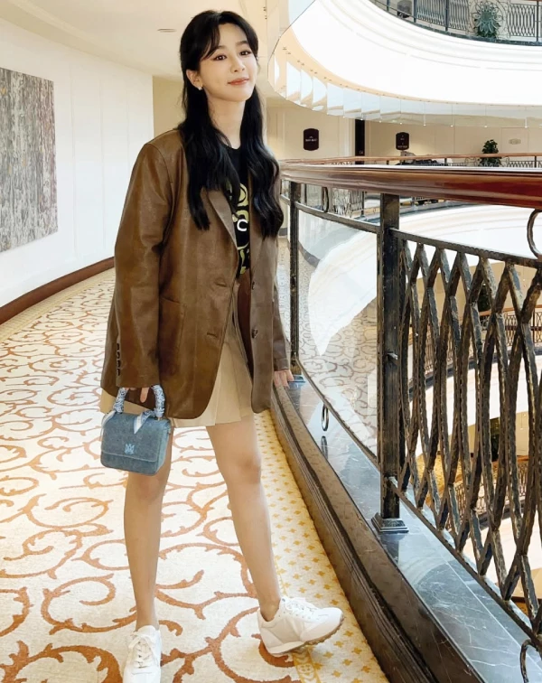楊紫的這身穿搭,成功將學院風與復古風巧妙融合,展現出率性又帶點文藝感的時尚氛圍。寬大的棕色皮革西裝外套,成為此整體造型的核心亮點,復古質感濃厚,不僅增添氣場,也讓穿搭更具個性。內搭簡約的黑色T恤,利用深色系平衡皮革外套的存在感,更加俐落耐看。下身搭配卡其色百褶短裙,則瞬間注入一股青春氣息,帶出學院風特有的活力感。