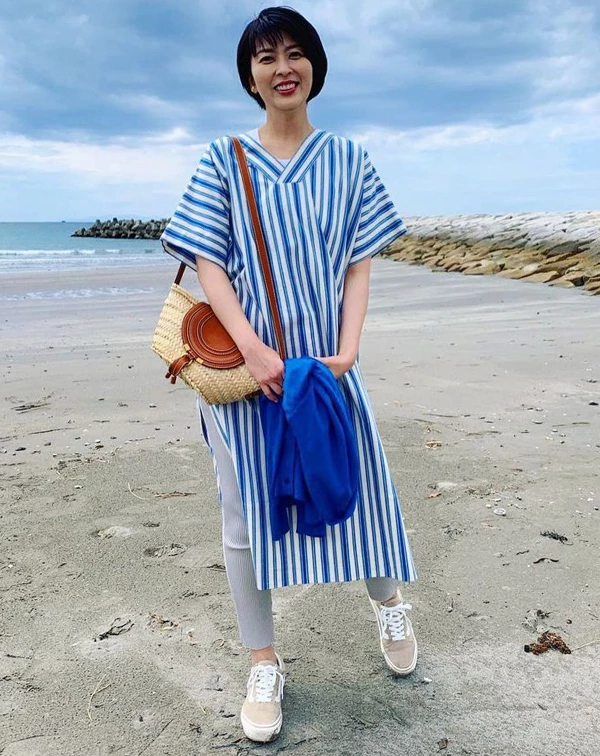 站在海邊的松隆子,選擇了最能代表清爽感的海軍藍與白色交錯的直條紋寬鬆長洋裝,側邊開衩的設計,隱約露出內搭的淺灰色羅紋緊身褲與休閒帆布鞋。「藍、白配」,可說是視覺減齡法當中,最萬年不敗的黃金公式。這是,只要手上隨性抓著同色系的藍色針織外套,再斜背一個皮革拼接草編包,便能瞬間注入滿滿的空氣感與悠閒少女氣息,完全打破我們對於50歲就是長者的沉悶感喔!