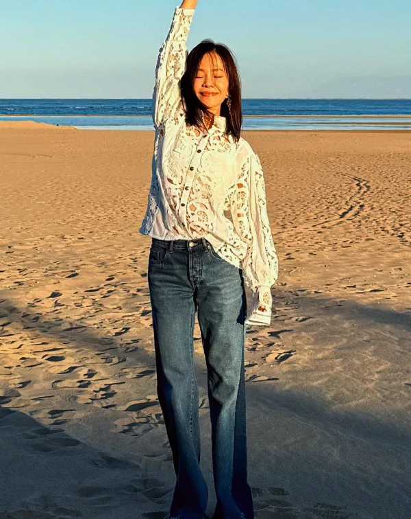 來到海邊,一件全白鏤空蕾絲長袖襯衫,隨風飄動時若隱若現;下半身只需要一條版型極佳的高腰微喇叭牛仔褲,就把腿型修飾得又長又直。這種大方、乾淨的極簡搭配,就是最自然的凍齡配方。