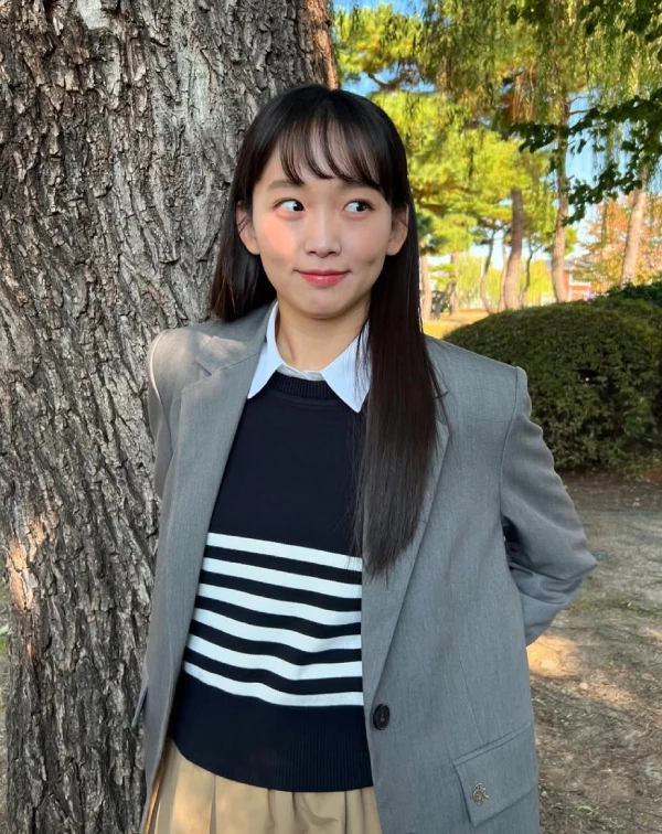 許多人擔心灰色西裝外套會顯老，但秦基周卻在裡面內搭了一件條紋針織衫及白色襯衫，直接打破西裝的沉悶感，下半身配上卡其色裙裝，完美平衡了正式與休閒，不僅是高級的微甜職場穿搭，還能給人一種專業度不減，且充滿朝氣的時髦印象。