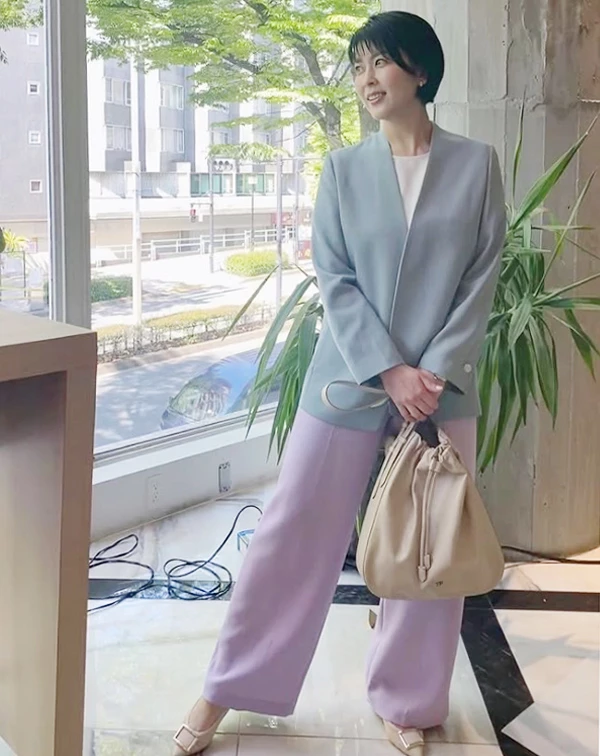 誰說過50歲就不能穿彩色?這套搭配絕對是熟齡女性一定要學起來的「高階色彩減齡術」! 照片中,松隆子打破了職場正裝非黑即白的沉悶框架,大膽將兩種柔和的馬卡龍色系疊加。無領設計的灰藍色西裝外套,內搭純白上衣,下身則大膽配上一條薰衣草紫的寬褲。
