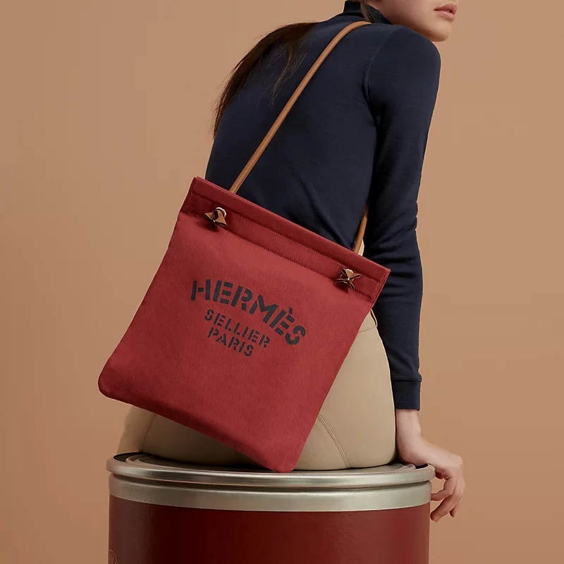 愛馬仕Groom包以人字紋帆布打造，配上Swift小牛皮肩帶、馬鞍針縫與「Hermès Sellier Paris」圖紋印花，源自品牌馬術系列，法國製造。