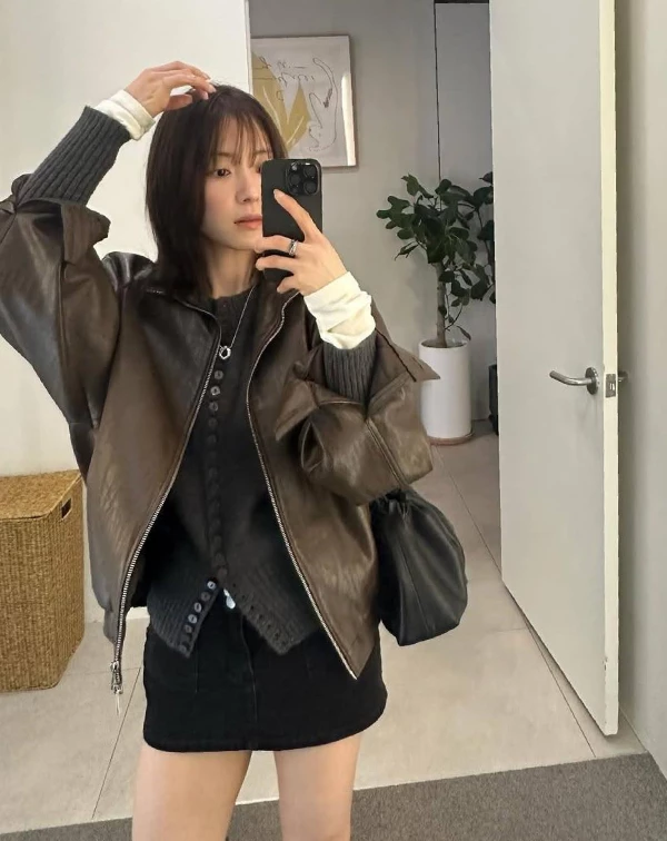李世榮用一件復古感的咖啡色皮外套作為主角，內搭黑色排釦上衣與短裙，打造出俐落又顯腿長的全黑基底，再透過袖口微微露出的白色內搭增加層次亮點，讓整體不會過於沉重。皮革的率性感中和了短裙的甜美，搭配隨性手拎的黑色包款，多了一點不經意的時髦感，看起來就像隨手一拍都很有態度。
