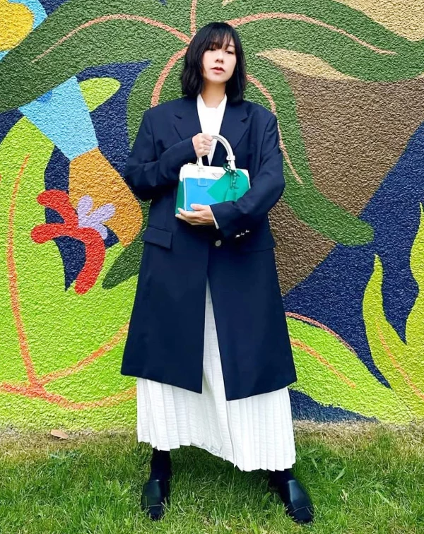 像這種「長+長」的服裝單品搭配,非常適合想藏肉又有氣場的姐姐們。我們可以挑一件長度蓋過臀部的微Oversize外套;下面搭一條材質輕盈(如雪紡或細褶)的長裙。西裝的挺拔,能把上半身線條收得很好,下半身的白色裙擺隨風飄動又不會顯得沉重。最後記得,包包一定要選個帶有撞色或亮色系的款式,一抹亮點,就能讓妳在優雅中帶點不落俗套的時髦趣味!