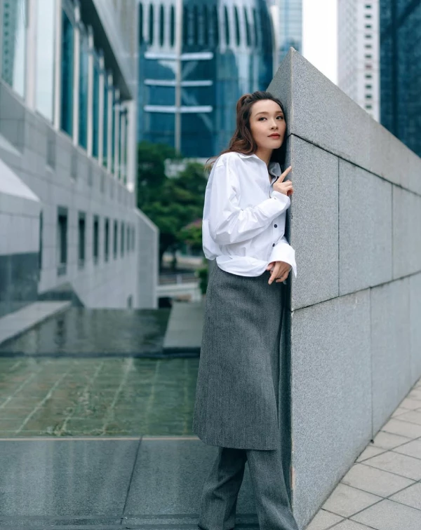 李佳芯完美演繹了什麼叫作走在時尚前端的「高智感逆齡」。我們平常穿白襯衫配西裝褲總覺得太嚴肅，快學她這招進階步驟！先穿上一件俐落的寬版剪裁白襯衫，下半身大膽嘗試「裙褲疊穿」—在灰色西裝寬褲外面，再疊加一條同色系的一片裙。這個技巧，能瞬間打破中規中矩的沉悶感。教學關鍵在於紮起一個高挺、帶有捲度的馬尾，把視覺重心向上拉，整個人不僅顯得高挑有精神，更散發出一股不用討好任何人的高級時髦感。