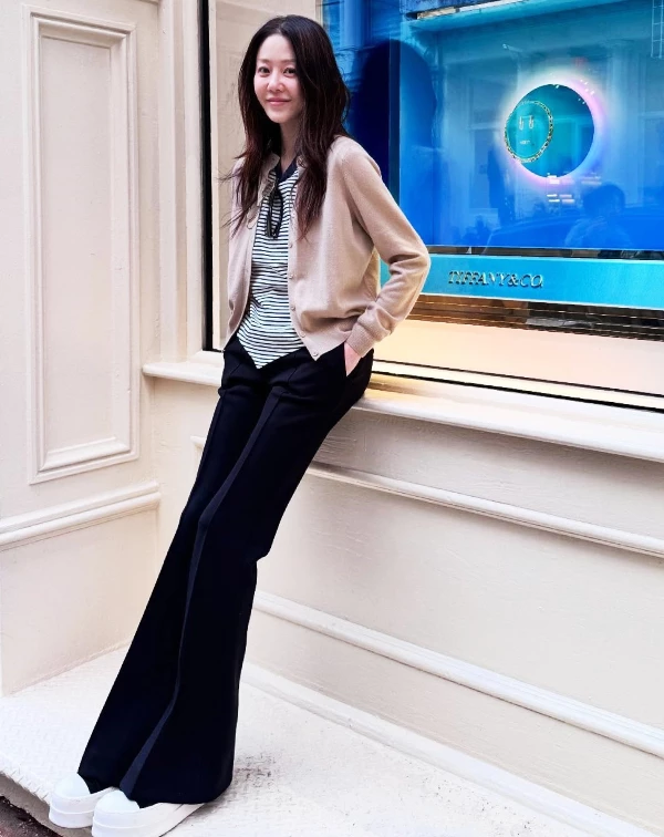高賢廷倚靠在Tiffany珠寶櫥窗前的私服照,完美詮釋了何謂「優雅的鬆弛感」,那抹淡雅、從容的笑容,完全呈現一種與歲月共行的自在氣息。至於穿搭上,高賢廷聰明地以溫柔的燕麥色針織衫,疊搭度假氣息的條紋內搭,並利用柔和的中性色調來提亮整體氣色,精準平衡溫潤與幹練;下半身,則是選用高腰的小喇叭寬褲,並搭配厚底小白鞋,不僅巧妙延伸長腿比例,更為整體造型注入如女大生般的清爽活力。