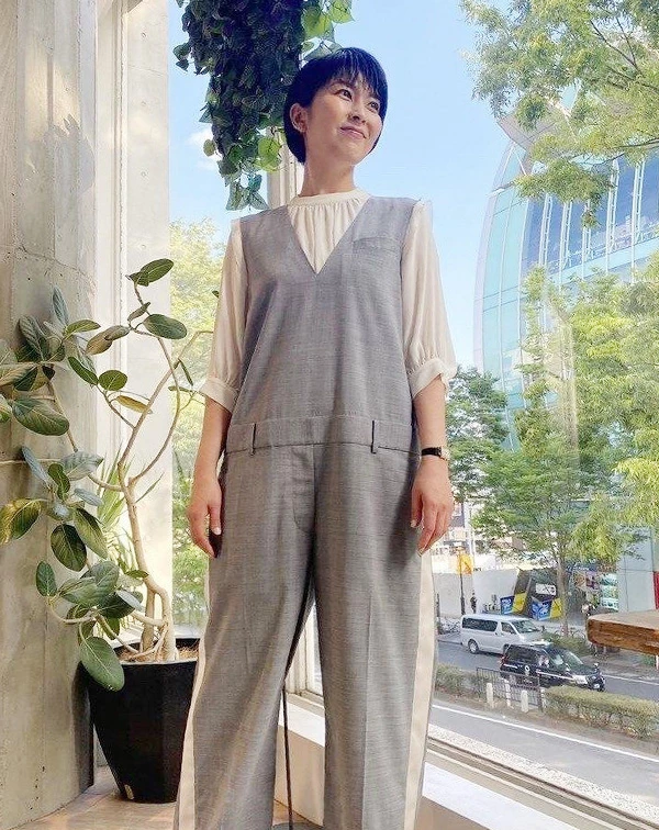 松隆子身穿一件深V剪裁的細緻灰色連身褲,內搭米白色微澎袖的雪紡襯衫。連身褲的兩側,帶有白色織帶的拼接細節,腰間則有類似西裝褲頭的設計,直接將工裝的率性與正裝的俐落完美結合。