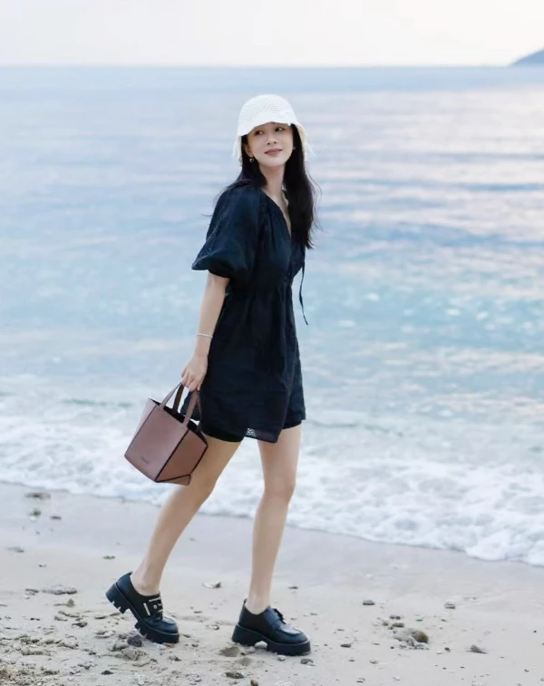 誰說去海邊只能穿長裙或比基尼?楊紫的這身私服穿搭,就完美示範了兼具質感與舒適的「時髦減齡」風格。她選擇一件帶有法式復古感的黑色澎袖短洋裝,微寬鬆的剪裁,在海風吹拂下顯得自然又隨性,同時巧妙修飾手臂線條,黑色系更在休閒氛圍中增添幾分低調優雅。而她沒有搭配常見的涼鞋,反而選擇黑色厚底樂福鞋作為混搭重點,硬挺鞋型與柔美洋裝形成反差感,瞬間提升整體時髦度。