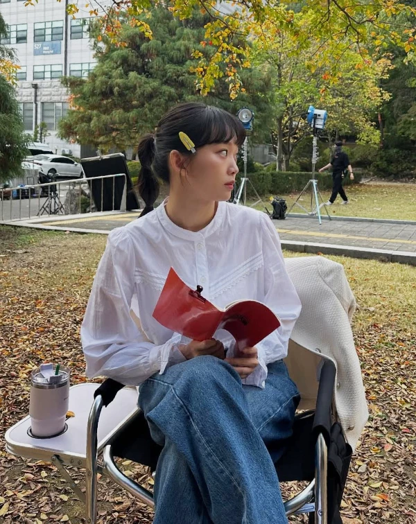 白襯衫加牛仔褲人人會穿，但秦基周聰明地挑選了帶有微宮廷風壓褶與小立領設計的白襯衫，少了上班族的嚴肅，多了幾分浪漫，瞬間把視覺年齡拉回20出頭。一般人日常在穿搭白襯衫時，可以捨棄過於合身、硬挺的正式版型，改選材質柔軟、帶有微落肩或精緻細節的款式。再配上一款亮色系的髮飾，就能輕鬆複製這種不費力的初戀感。