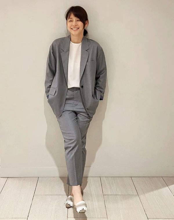 想讓西裝變年輕？不妨參考石田百合子的這套灰色西裝穿搭，示範了如何將正式感穿出「輕鬆感」，是職場女性非常值得參考的減齡中性風。她選用淺灰色成套的稍寬西裝，傳遞出一種不需要刻意展現身材曲線的從容氣度。而內搭，則是穿上純粹的圓領白T，像這種「西裝套裝 + 素T」的組合，瞬間就瓦解了容易顯得老氣或太過嚴肅的困擾，讓整體氛圍變得非常年輕且乾淨。利用低飽和度的中性色調，就能穿出像石田百合子一樣，既有質感又充滿活力的知性美！